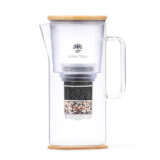 Eine Glas-Wasserfilterkanne von Lotus Vita mit Bambusdeckel, die den mehrschichtigen Filter im Inneren zeigt.