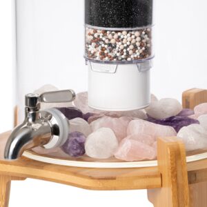Nahaufnahme eines Glas-Wasserfiltersystems mit mehrstufiger Filterkartusche, die auf einem Bett aus Rosenquarz- und Amethyst-Kristallen ruht.