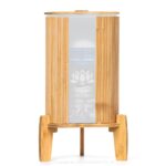 Ein Stand-Wasserfilter mit 8 Litern Fassungsvermögen, umhüllt von einem Lichtschutz aus Bambus, stehend auf einem passenden Bambussockel.