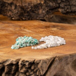 Zwei Haufen getrommelter Edelsteine, türkisfarbener Amazonit und weißer Milchopal, auf einer rustikalen Holzoberfläche.