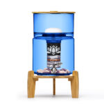 Eleganter Stand-Wasserfilter aus blauem Glas mit Bambus-Elementen, der die inneren Filterschichten und Edelsteine zeigt.
