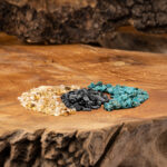 Drei verschiedene Edelsteinmischungen – Goldener Beryll, Turmalin und Türkis – liegen auf einer rustikalen Holzoberfläche.