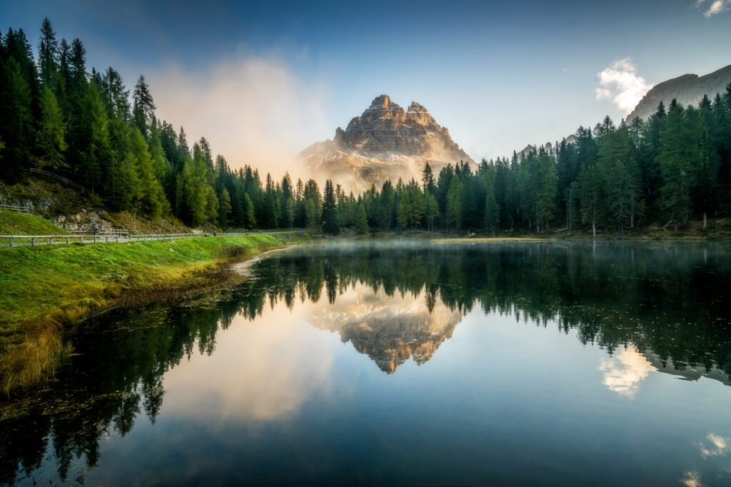 Ein klarer Bergsee, in dem sich die majestätischen Dolomiten und ein dichter Nadelwald bei Sonnenaufgang spiegeln.