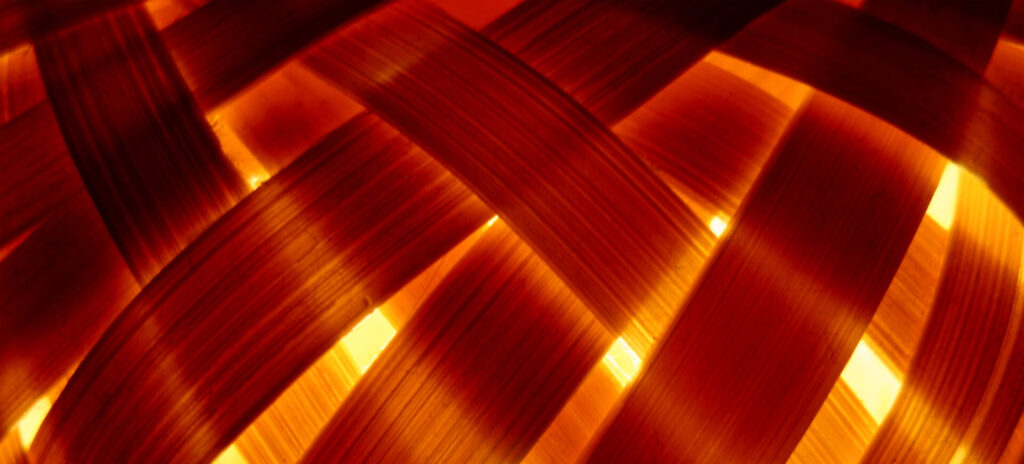 Nahaufnahme von beleuchtetem, orange-farbenem Bambusgeflecht als Symbol für natürliche Materialien.