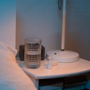 Ein Glas Wasser steht neben einem Bett auf einem Nachttisch, um das Thema der Wasserqualität über Nacht zu illustrieren.