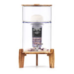 Eleganter Glas-Wasserfilter mit mehrstufiger Filtertechnologie, Deckel aus Akazienholz und einem passenden Holzgestell, veredelt mit Edelsteinen am Boden.